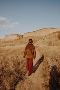 Rear view of woman walking on dirt road against sky