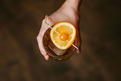 From above of crop anonymous person with glass of whiskey with ice cubes and stick with orange and berry person