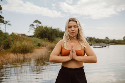 Portrait of young woman with arms raised against lake