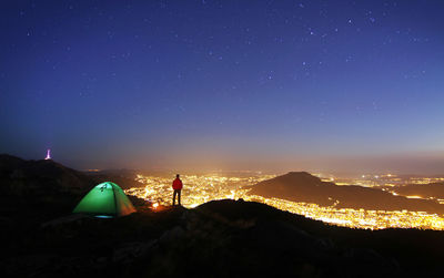 Rear view of man looking at illuminated city while standing on mountain