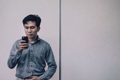 Man wearing shirt using phone while standing against wall