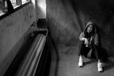 Woman wearing hooded shirt sitting against wall