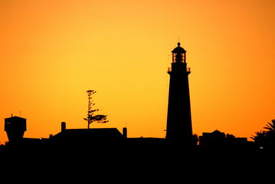 Low angle view of silhouette lighthouse against orange sky