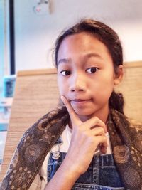 Close-up portrait of cute teenage girl with hand on chin at home