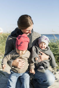 Woman carrying daughters on beach against clear sky