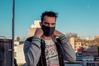 Portrait of young man with face mask in city against clear sky