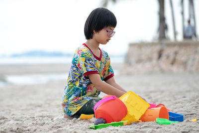 Side view of girl with toy playing on sandy beach