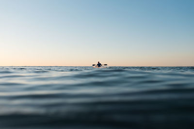 Man in sea against sky during sunset