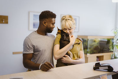 Woman embracing dog by man at reception in veterinary clinic