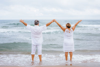 Rear view of friends standing at beach against sky