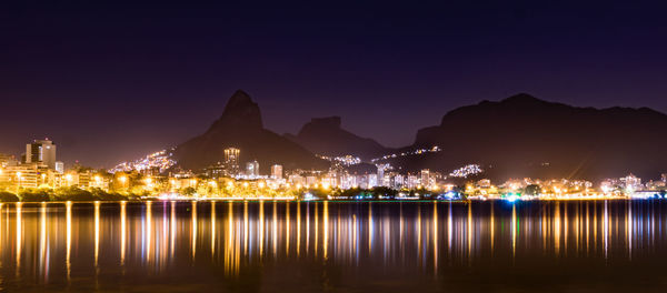 Illuminated city by river against sky at night