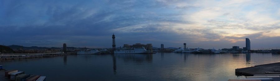 City by river against sky during sunset