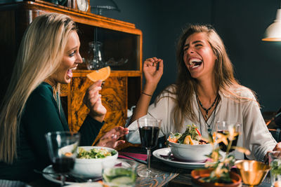 Female friends laughing while having food and drinks at table