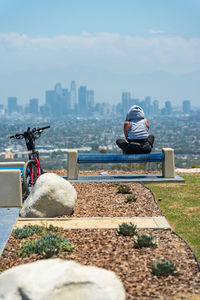 Woman sits on bench and looks at la city scape after a long bike ride