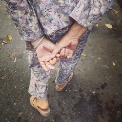 Low section of woman with hands clasped walking on road