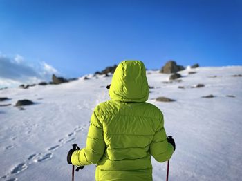 Rear view of woman wearing green hooded winter coat hiking alone in the mountains