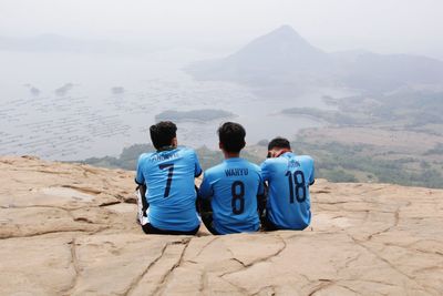 Rear view of friends sitting on mountain against sky