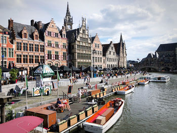 Boats in river by buildings in city against sky