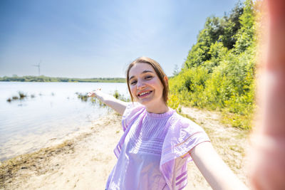 Portrait of young woman standing against lake