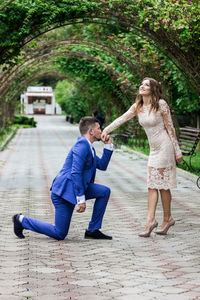 Man kissing on woman hand over footpath against trees