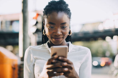 Young woman smiling while using smart phone on street in city