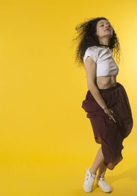 Young woman looking away against yellow background