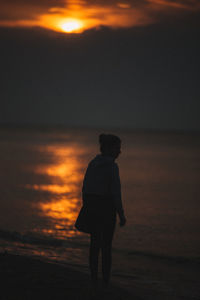 Silhouette man standing on beach against orange sky