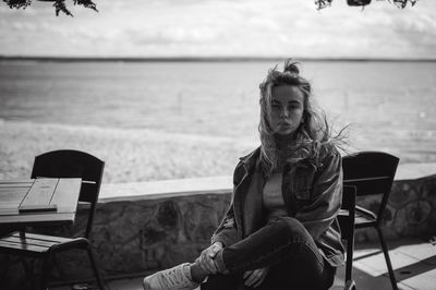 Portrait of young woman sitting on chair at beach