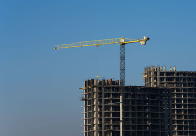 Low angle view of crane by building against clear blue sky