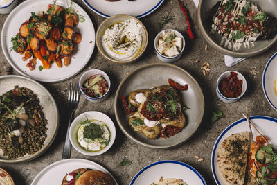 From above of various eastern dishes and snacks arranged with sauces and cutlery on gray surface