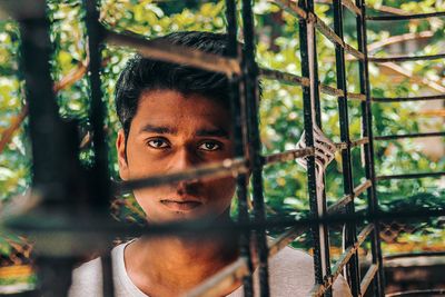 Portrait of young man seen through metal fence