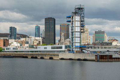 Modern buildings by river against sky in city