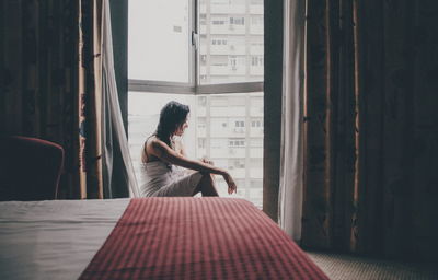 Side view of woman standing by window at home