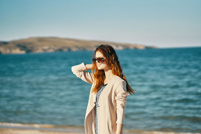 Woman wearing sunglasses standing by sea against sky