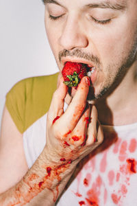 Close-up of man eating strawberry against white background 