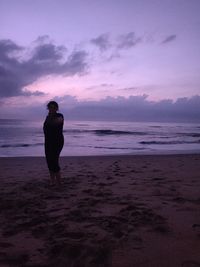 Rear view of man standing on beach against sky during sunset