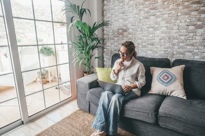 Portrait of woman using mobile phone while sitting on sofa at home