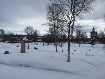 Bare trees on snow covered landscape against sky