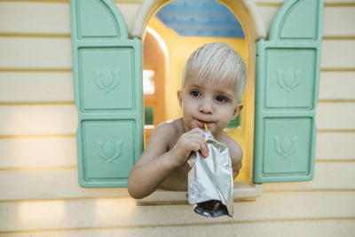 Close-up of boy having drink while looking through window in playhouse