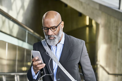 Businessman with smartphone reading messages on escalator