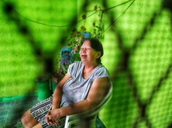 Smiling senior woman sitting on chair seen through fence