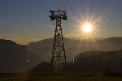 Low angle view of overhead cable car tower on field against sky during sunset