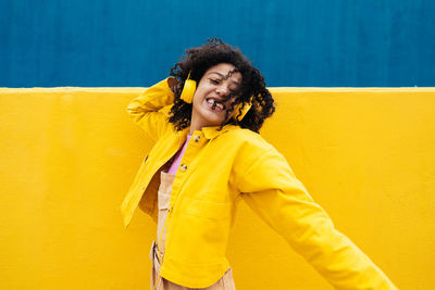 Young woman standing against yellow wall