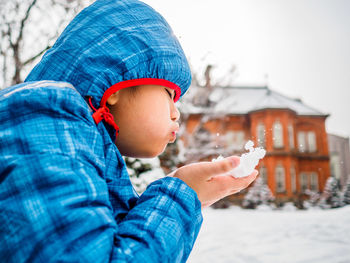 Side view of boy playing with snow while sitting outdoors