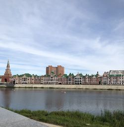 View of buildings by river against cloudy sky