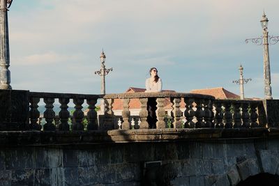 Woman in sunglasses standing on bridge against sky