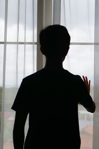 Rear view of silhouette woman standing against window at home