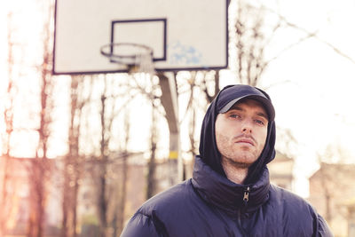 Portrait of young man standing against basketball hoop and trees