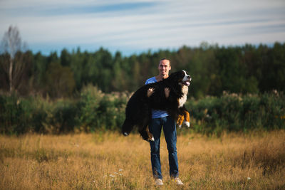 Portrait of man carrying dog while standing on grassy land