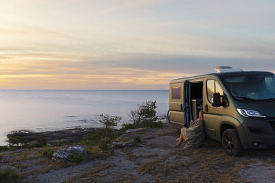 Woman sitting near motorhome and looking at sea